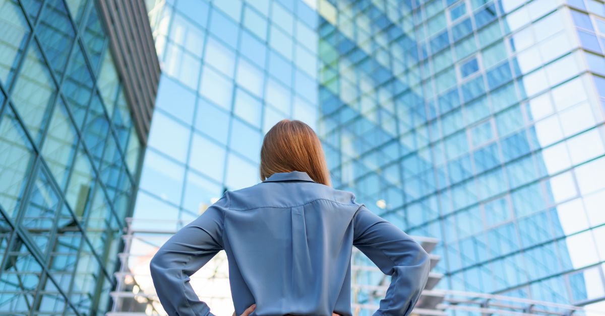 Woman in blue shirt standing akimbo among the all-glasses skyscrapers